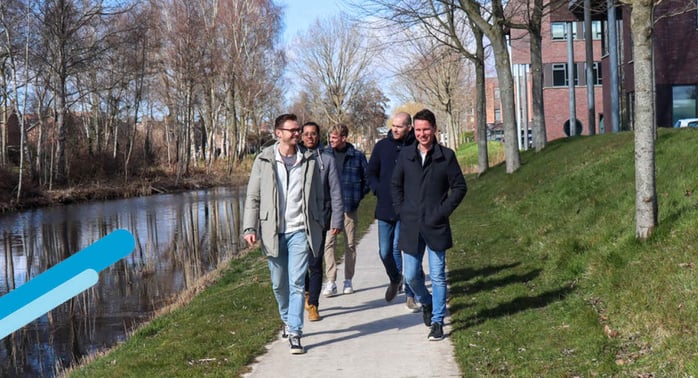 Een groep van 5 mensen wandelen over een pad langs het water